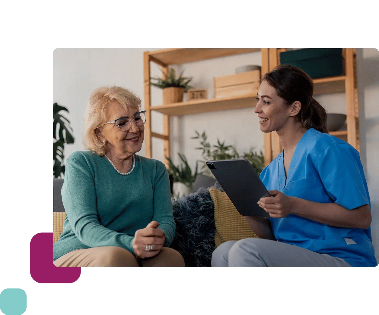 Female nurse holding tablet sat with elderly woman